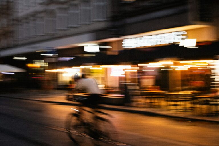 Blurred cyclist rides past illuminated storefronts at night